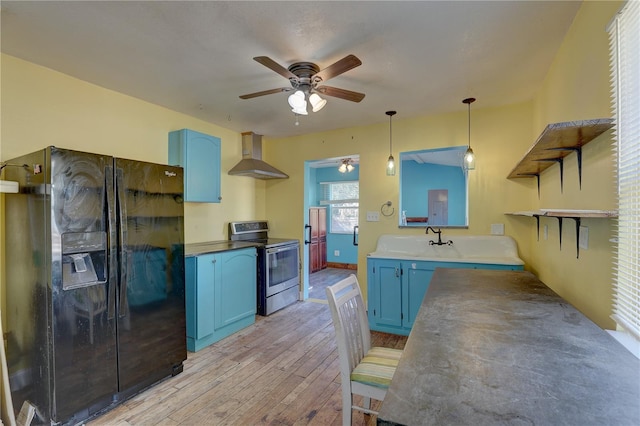 kitchen with electric stove, wall chimney range hood, blue cabinets, decorative light fixtures, and black refrigerator with ice dispenser