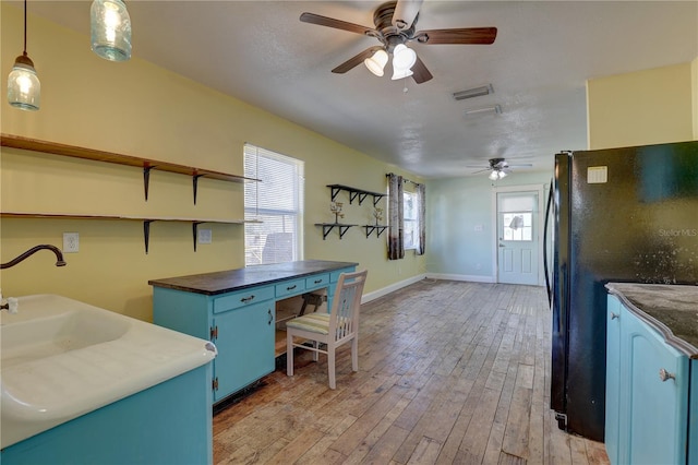 kitchen featuring blue cabinets, black fridge, pendant lighting, ceiling fan, and light hardwood / wood-style floors