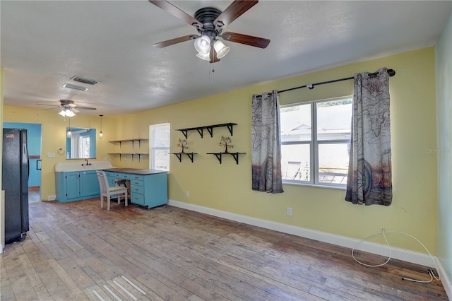 kitchen with blue cabinets, sink, black fridge, a textured ceiling, and light hardwood / wood-style floors