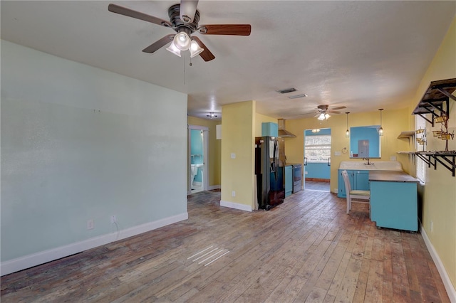 kitchen with pendant lighting, wood-type flooring, ceiling fan, kitchen peninsula, and black fridge