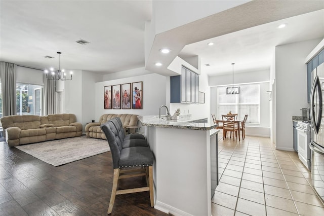 kitchen featuring a kitchen breakfast bar, kitchen peninsula, a notable chandelier, dark stone counters, and white gas range oven