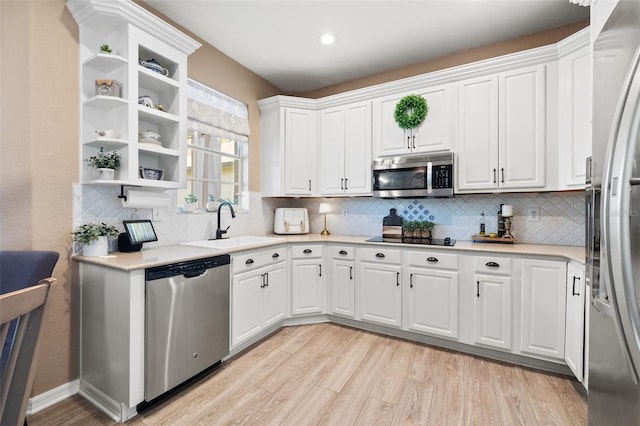 kitchen featuring appliances with stainless steel finishes, white cabinetry, sink, backsplash, and light wood-type flooring