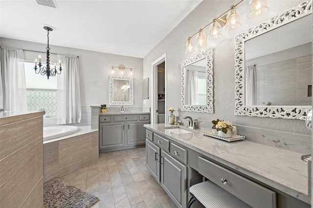 bathroom with vanity, tiled tub, and an inviting chandelier