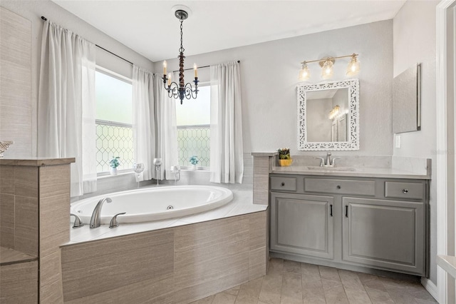 bathroom with vanity, a relaxing tiled tub, a wealth of natural light, and an inviting chandelier