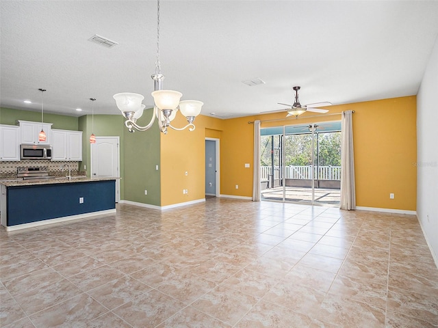 interior space featuring ceiling fan with notable chandelier, pendant lighting, white cabinetry, backsplash, and light stone counters