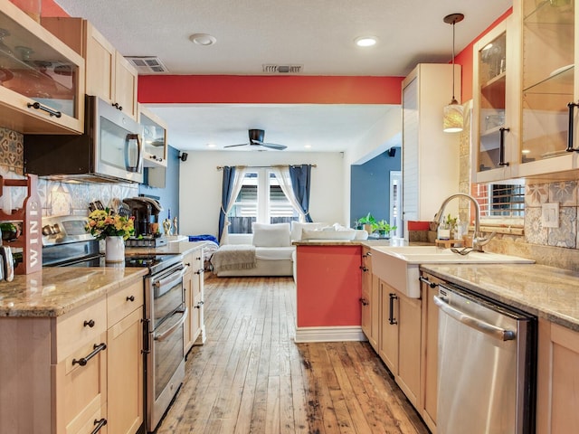 kitchen with appliances with stainless steel finishes, pendant lighting, light brown cabinetry, sink, and light wood-type flooring