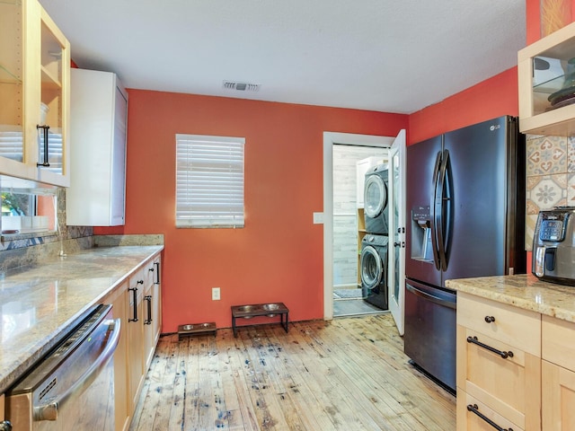 kitchen with dishwasher, stacked washer and dryer, light stone counters, fridge with ice dispenser, and light hardwood / wood-style flooring