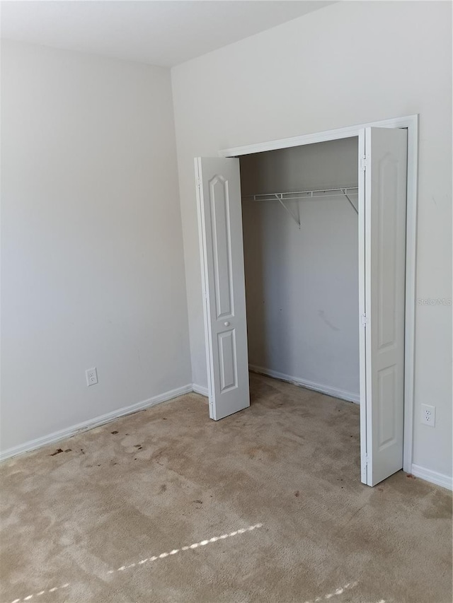 unfurnished bedroom with light colored carpet and a closet