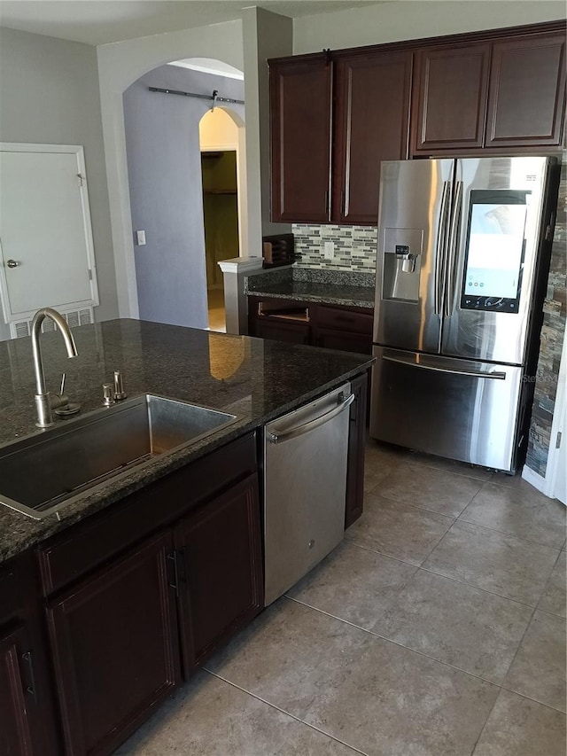 kitchen featuring sink, dark stone countertops, backsplash, stainless steel appliances, and dark brown cabinets