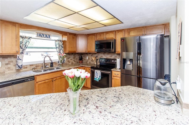 kitchen featuring appliances with stainless steel finishes, light stone countertops, sink, and decorative backsplash