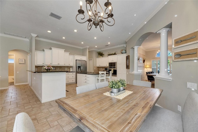 dining space with crown molding, an inviting chandelier, a textured ceiling, and ornate columns