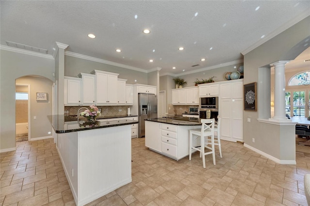 kitchen with decorative columns, a breakfast bar area, white cabinets, black appliances, and a spacious island