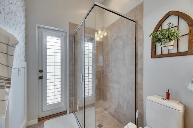 bathroom featuring a shower with shower door, toilet, and a healthy amount of sunlight