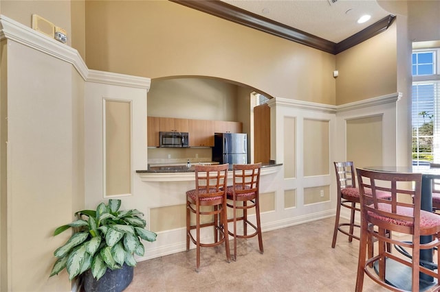 kitchen with stainless steel refrigerator, a towering ceiling, ornamental molding, and a kitchen breakfast bar