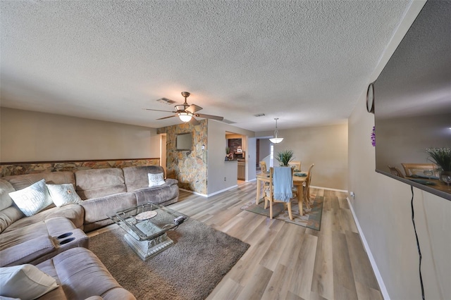 living room with ceiling fan, a textured ceiling, and light wood-type flooring