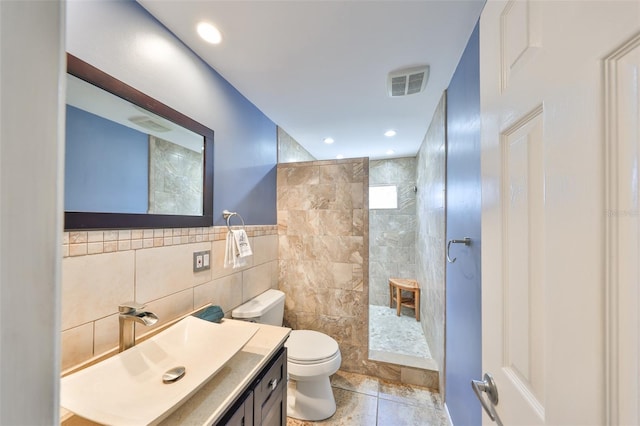 bathroom with tile patterned floors, toilet, tile walls, a tile shower, and vanity