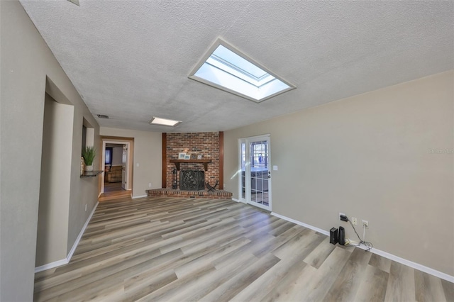 unfurnished living room featuring a brick fireplace, a textured ceiling, light hardwood / wood-style floors, and a skylight