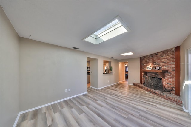 unfurnished living room with a brick fireplace, light hardwood / wood-style flooring, and a skylight