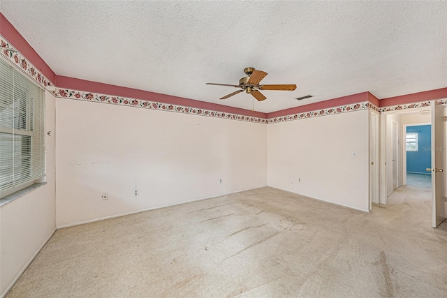 spare room featuring ceiling fan, light colored carpet, and a textured ceiling