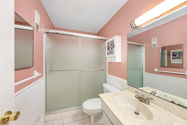 bathroom with a shower with door, vanity, a textured ceiling, tile patterned floors, and toilet