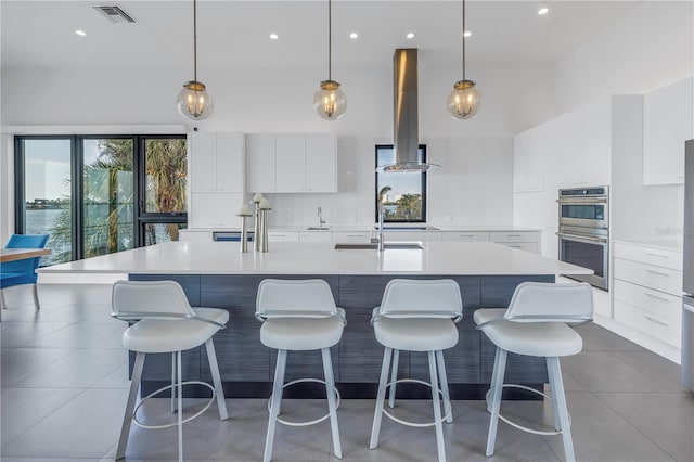 kitchen with white cabinets, ventilation hood, double oven, and a large island with sink