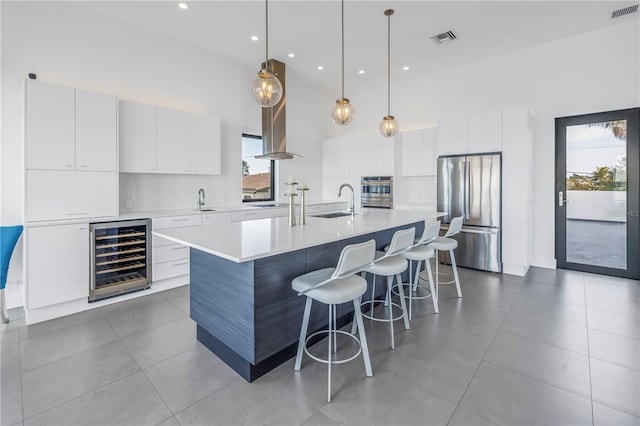 kitchen with white cabinetry, beverage cooler, hanging light fixtures, stainless steel appliances, and a center island with sink