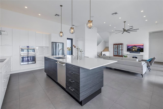 kitchen featuring pendant lighting, appliances with stainless steel finishes, a towering ceiling, white cabinets, and a large island with sink