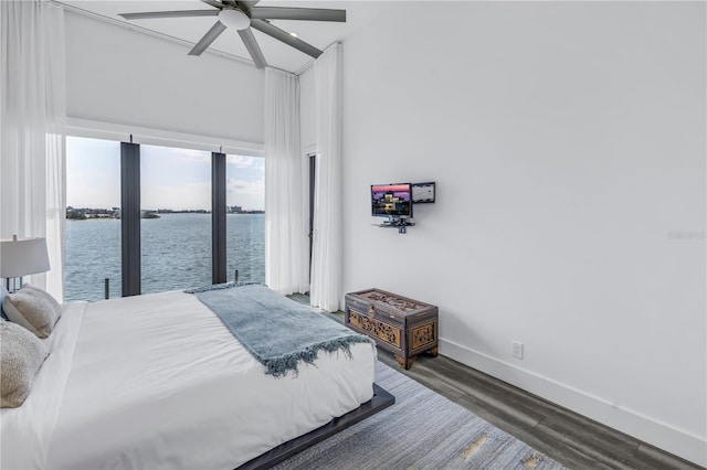 bedroom with dark hardwood / wood-style flooring, ceiling fan, and a water view