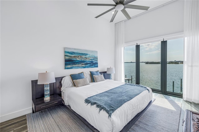 bedroom with access to outside, dark hardwood / wood-style floors, ceiling fan, and a water view