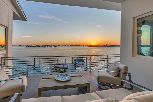 patio terrace at dusk featuring outdoor lounge area, a balcony, and a water view