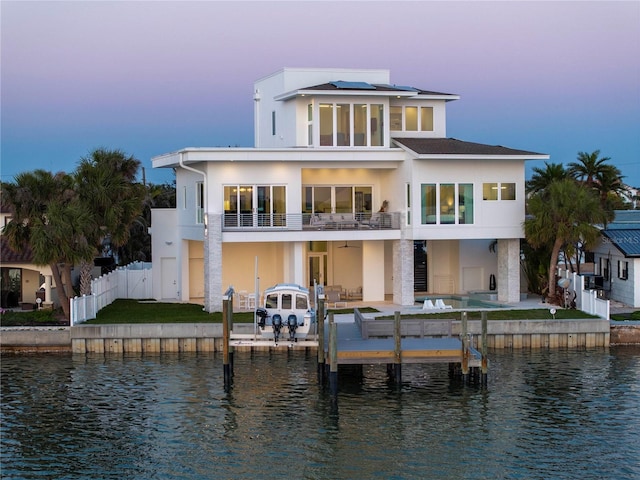 back house at dusk with solar panels, a patio area, a balcony, and a water view