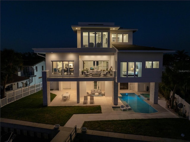 back house at night featuring a fenced in pool, a yard, a patio area, solar panels, and a balcony