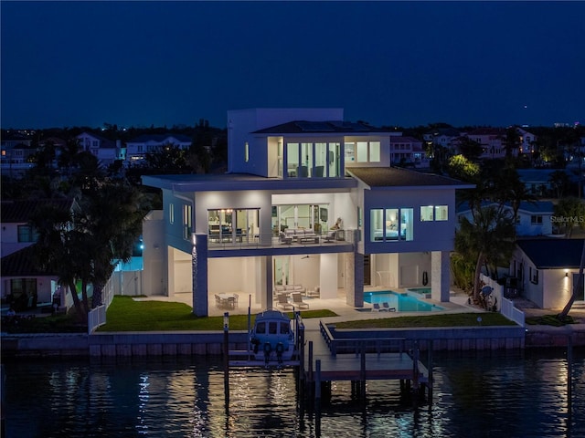 back house at twilight with a water view, a balcony, a fenced in pool, and a patio area