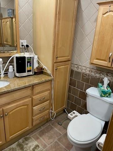 bathroom featuring vanity, tile walls, and toilet