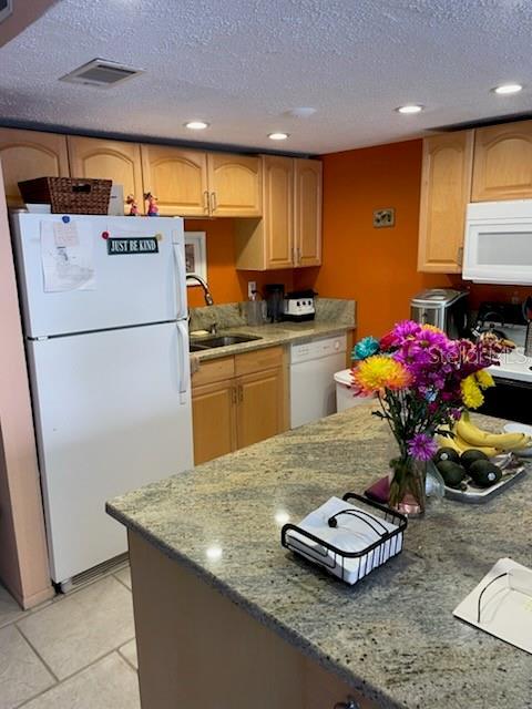 kitchen featuring sink, a textured ceiling, light tile patterned floors, white appliances, and light stone countertops