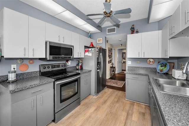 kitchen with appliances with stainless steel finishes, sink, white cabinets, and light hardwood / wood-style flooring