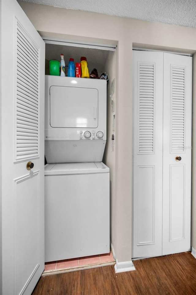 clothes washing area featuring stacked washer / drying machine, a textured ceiling, and dark hardwood / wood-style flooring