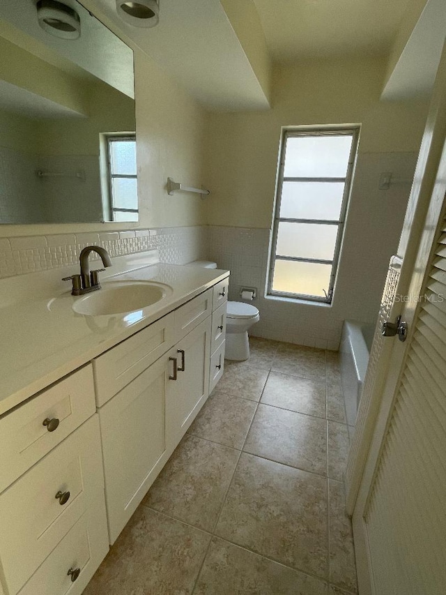 bathroom with toilet, tile walls, vanity, a bathtub, and tile patterned flooring