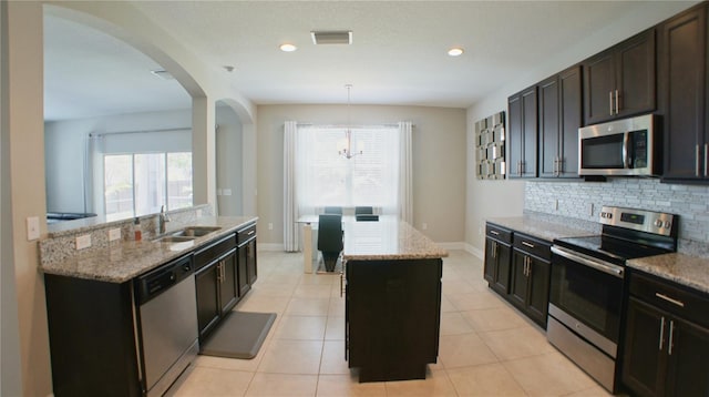 kitchen featuring sink, appliances with stainless steel finishes, hanging light fixtures, light stone countertops, and a center island with sink