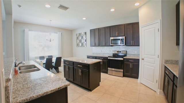 kitchen with sink, decorative light fixtures, an island with sink, stainless steel appliances, and light stone countertops