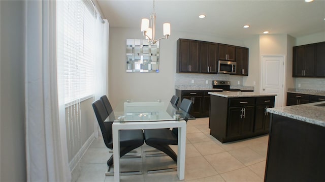 kitchen featuring tasteful backsplash, dark brown cabinets, hanging light fixtures, light tile patterned floors, and stainless steel appliances