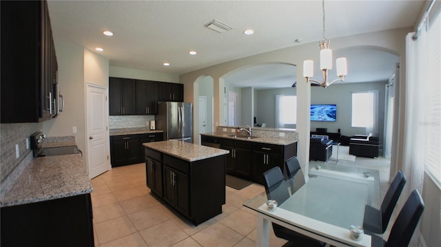 kitchen featuring light tile patterned floors, stainless steel refrigerator, range, a kitchen island, and decorative light fixtures