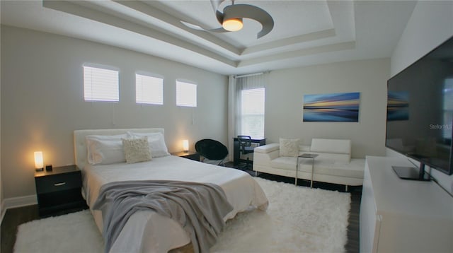 bedroom with ceiling fan, wood-type flooring, and a raised ceiling