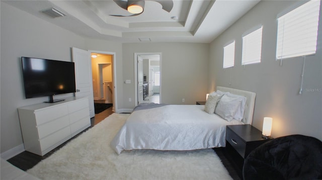 bedroom with a raised ceiling, connected bathroom, and ceiling fan