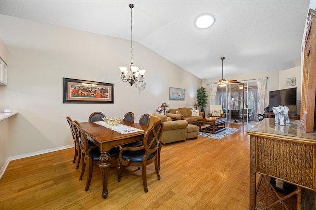 dining room featuring ceiling fan with notable chandelier, vaulted ceiling, and light wood-type flooring