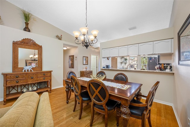 dining space featuring vaulted ceiling, a chandelier, and light hardwood / wood-style flooring