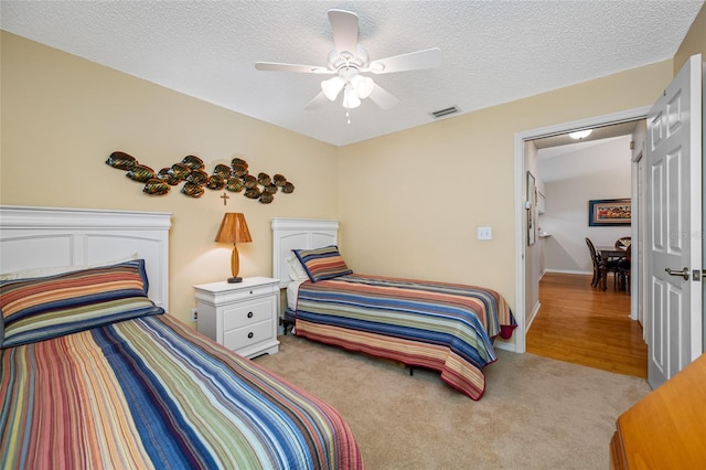 bedroom with ceiling fan, light colored carpet, and a textured ceiling