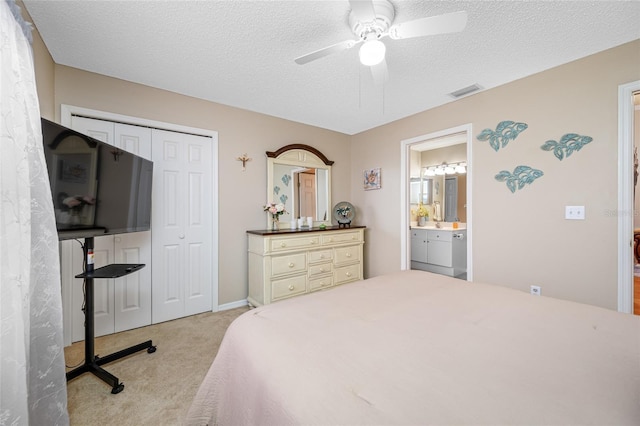 bedroom featuring ceiling fan, ensuite bathroom, a textured ceiling, light carpet, and a closet