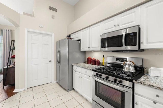 kitchen featuring light tile patterned flooring, light stone countertops, white cabinets, and appliances with stainless steel finishes