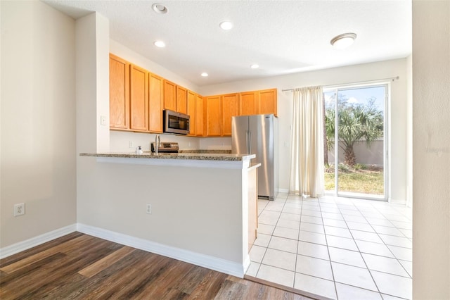 kitchen with stainless steel appliances, light stone countertops, kitchen peninsula, and light hardwood / wood-style flooring